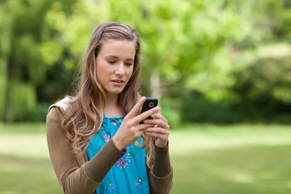 Menina adolescente séria enviando um texto enquanto estava em um parque — Fotografia de Stock