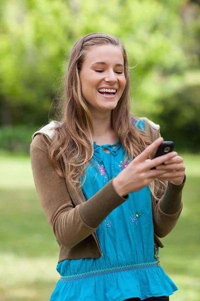 Adolescente riendo mientras recibe un mensaje de texto en su teléfono celular — Foto de Stock