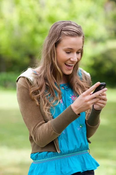Feliz adolescente recibiendo un mensaje de texto en su teléfono celular mientras está de pie — Foto de Stock