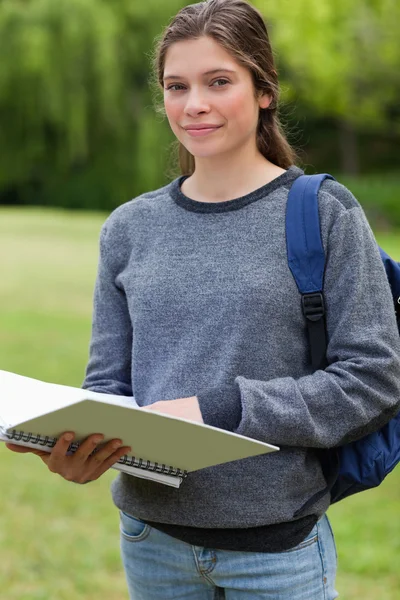 Young relaxed girl holding her notebook while carrying her backp — Stock Photo, Image