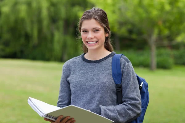 Молодая счастливая девушка держит свой блокнот в парке, показывая — стоковое фото