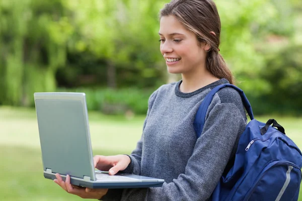 Junge lächelnde Frau hält ihren Laptop in der Hand, während sie ihren Backpa trägt — Stockfoto