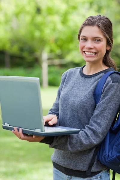 Улыбающаяся молодая девушка держит свой ноутбук, глядя на камеру — стоковое фото