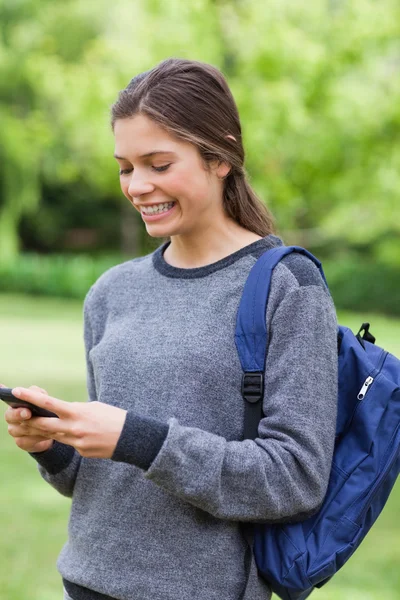Usměvavá mladá dívka odesílá text s mobilním telefonem — Stock fotografie