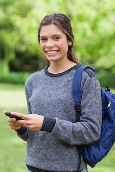 Smiling teenage girl standing upright while sending a text — Stock Photo, Image