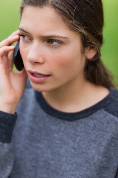 Молодая серьезная девушка разговаривает по телефону, глядя в сторону — стоковое фото