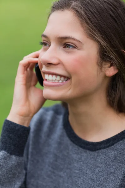 Joven chica sonriente llamando con su teléfono celular mientras está de pie — Foto de Stock
