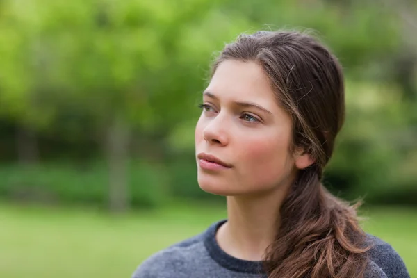 Młoda kobieta stoi w parku, patrząc w kierunku — Zdjęcie stockowe