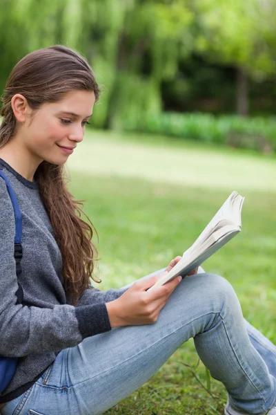 年轻微笑的女人坐在草地上读一本书 — 图库照片