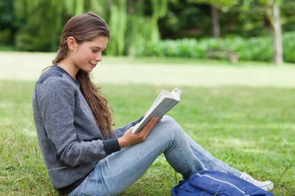 Молодой расслабленный взрослый читает книгу, сидя на траве — стоковое фото