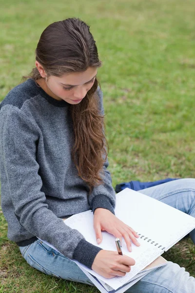 Молодая серьезная девушка делает уроки, сидя на траве — стоковое фото
