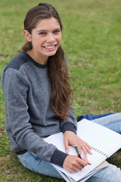 Sonriente joven escribiendo en su cuaderno mientras mira el — Foto de Stock