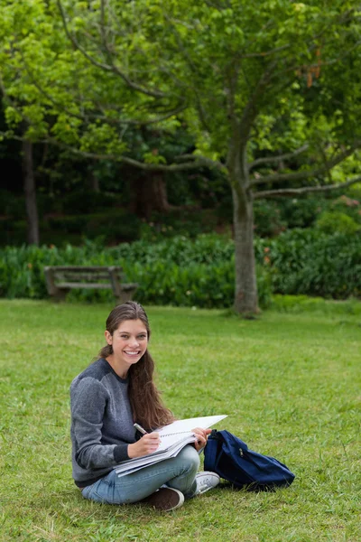 Smiling teenage girl doing her homework while sitting down in a — Stock Photo, Image
