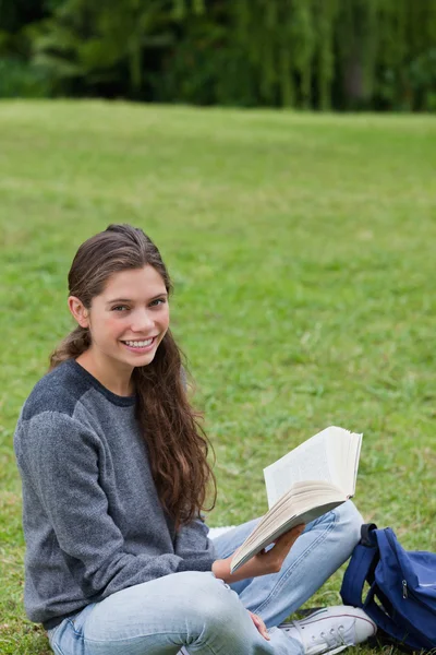 Joven chica sonriente sentada con las piernas cruzadas mientras sostiene un libro —  Fotos de Stock