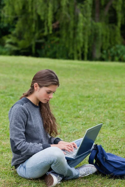 Vážné mladá žena psaní na svém laptopu, zatímco sedí mezi nohy — Stock fotografie