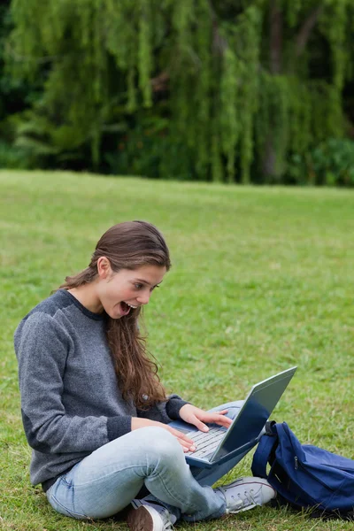 Удивлена, что молодая девушка смотрит на свой ноутбук, сидя на — стоковое фото