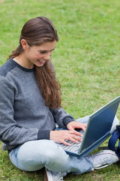 Lächelnde Studentin tippt auf ihrem Laptop, während sie sich auf den g setzt — Stockfoto