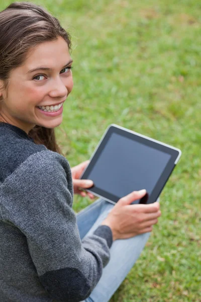 Young girl using her tablet pc while sitting down and showing a — Stock Photo, Image