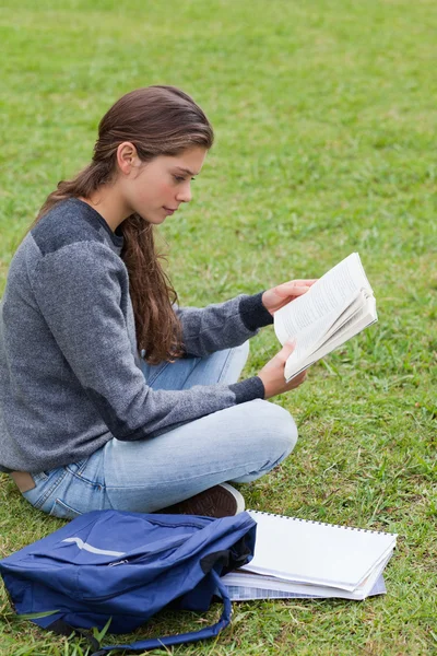 Joven chica seria leyendo un libro sentado con las piernas cruzadas —  Fotos de Stock