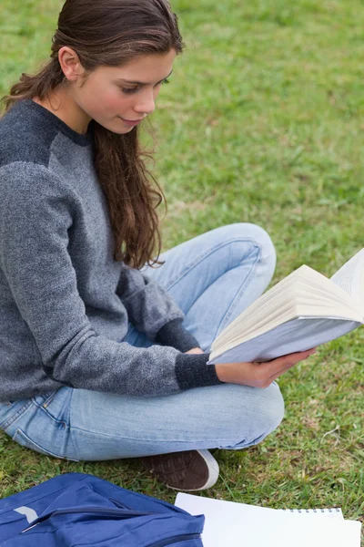 잔디에 앉아있는 동안 책을 읽고 편안 하 게 어린 소녀 — 스톡 사진