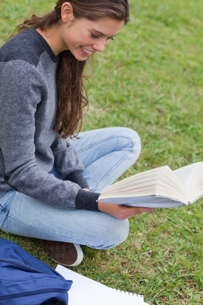 Молодая улыбающаяся женщина, держащая книгу, сидя со скрещенными ногами — стоковое фото