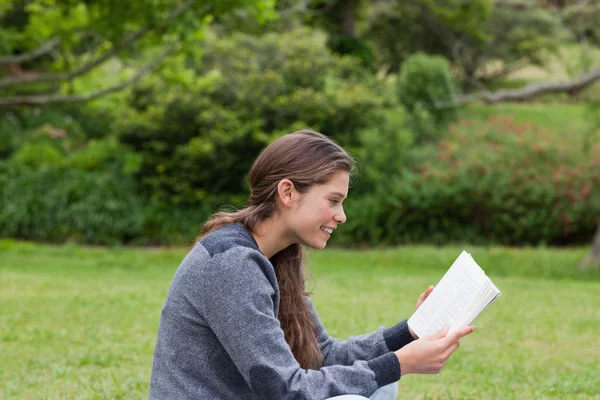 Side view of a young girl sitting cross-legged while reading a b — Stock Photo, Image
