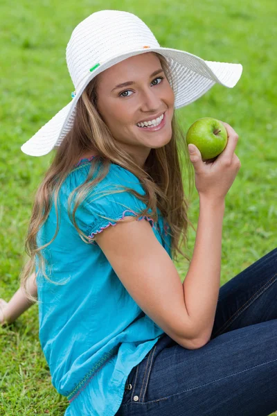 Jovem atraente sentada enquanto come uma maçã — Fotografia de Stock