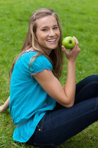 微笑着的年轻女子坐在票面时按住一个绿色苹果 — 图库照片