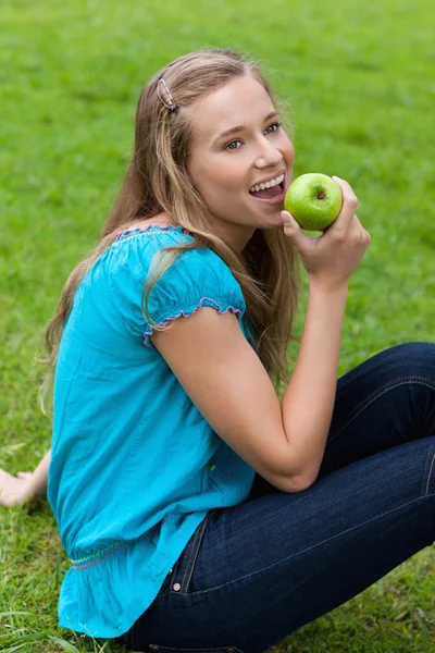Χαμογελώντας νεαρό κορίτσι τρώει ένα νόστιμο πράσινο μήλο, ενώ η συνεδρίαση — Φωτογραφία Αρχείου