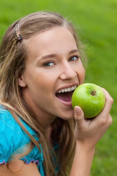 Молодая улыбающаяся женщина смотрит в камеру, когда ест яблоко — стоковое фото