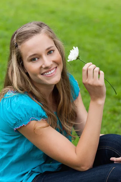 Giovane donna sorridente che tiene un fiore mentre si siede — Foto Stock