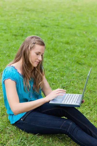 Jonge ontspannen vrouw met behulp van haar laptop zittend op het gras — Stockfoto