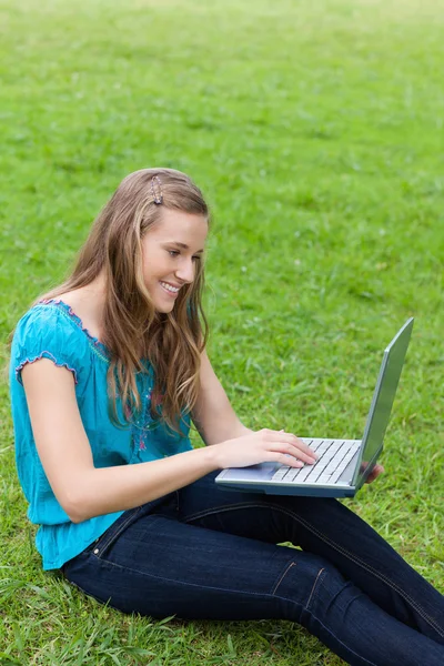 Young smiling girl typing on her laptop while sitting down on th — Stock Photo, Image