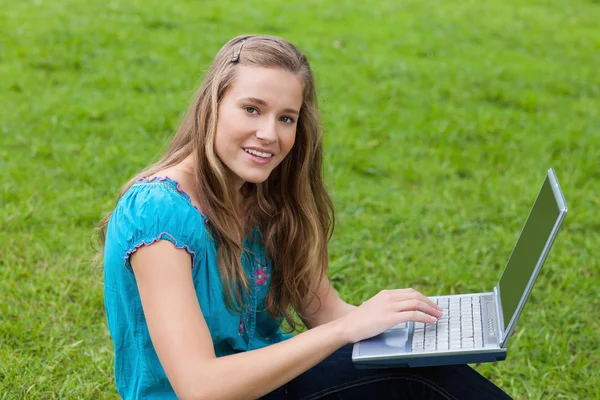 Chica joven usando su computadora portátil en un parque mientras mira al camer —  Fotos de Stock
