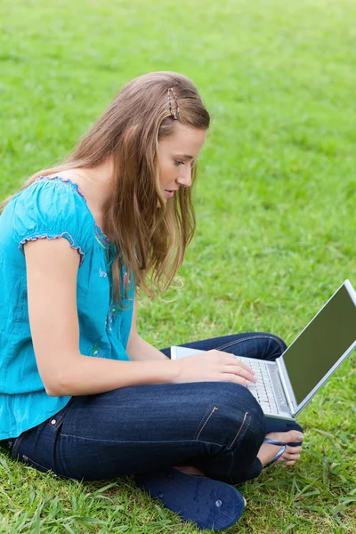 Young serious girl sitting cross-legged in a park while using he — Stock Photo, Image