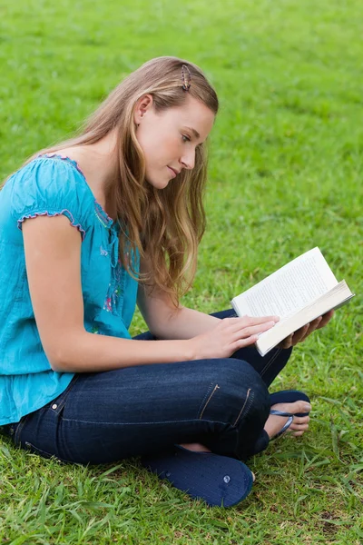 Серйозна молода дівчина читає книгу, сидячи в парку — стокове фото