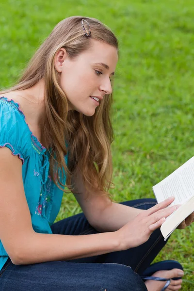 Menina atraente jovem sentado de pernas cruzadas em um parque enquanto readi — Fotografia de Stock