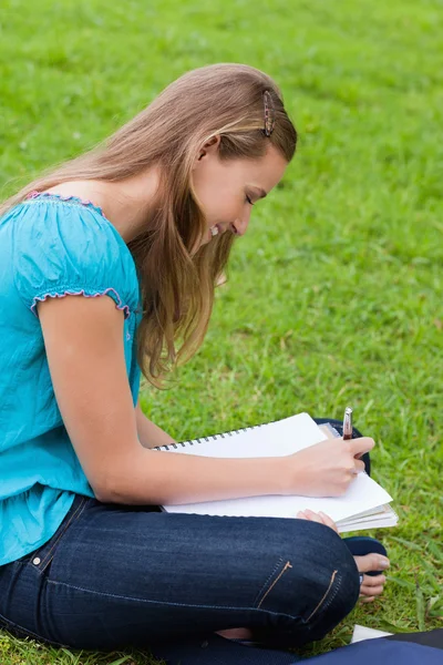Joven chica feliz haciendo su tarea mientras se sienta en el gr —  Fotos de Stock
