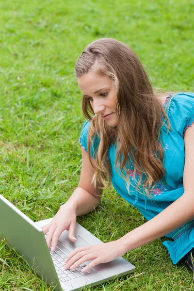 Junges ernstes Mädchen liegt auf dem Gras, während sie ihren Laptop benutzt — Stockfoto