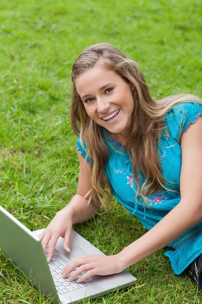 Smiling teenage girl lying on the side while using her laptop — Stock Photo, Image