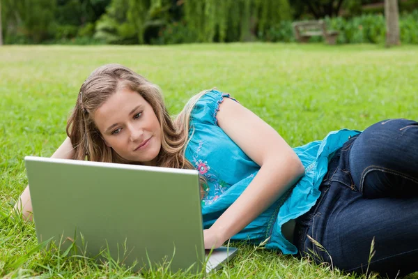 Smiling teenager lying on the grass with her hand on head while — Stock Photo, Image