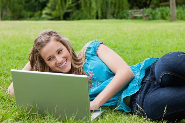 Junges lächelndes Mädchen, das auf der Seite in einem Park liegt, während es auf h tippt — Stockfoto