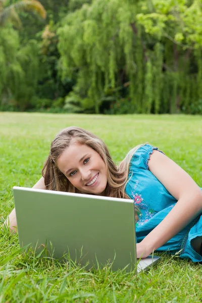 Menina sorrindo jovem usando seu laptop enquanto deitado na grama — Fotografia de Stock