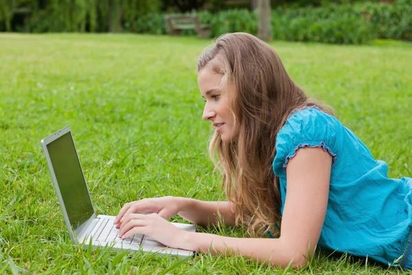 Sidovy av en ung flicka att skriva på sin laptop medan liggande — Stockfoto