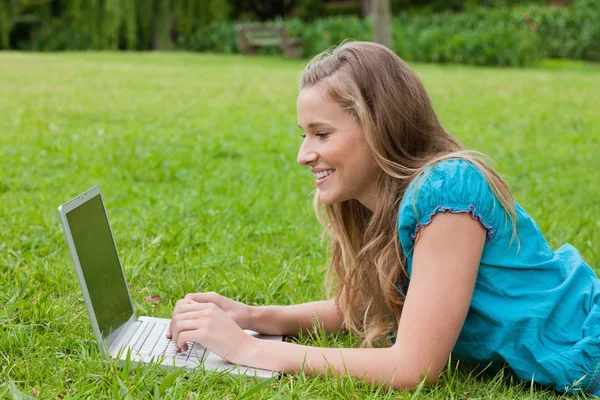 Νεαρό χαμογελαστό κορίτσι κοιτάζοντας το laptop της, ξαπλώνοντας — Φωτογραφία Αρχείου