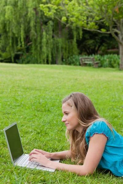 Вид сбоку на молодую девушку, работающую на ноутбуке, лежа на футболке — стоковое фото