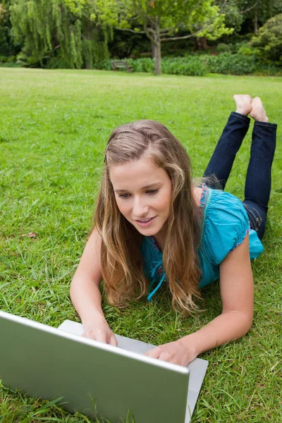Young girl lying on the grass while raising her legs and using h — Stock Photo, Image