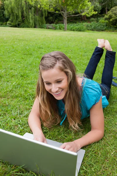 Étudiante souriante travaillant sur son ordinateur portable dans un parc tout en couchant avec — Photo