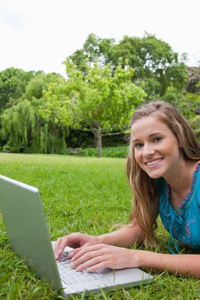 Smiling teenager looking at the camera while using her laptop — Stock Photo, Image