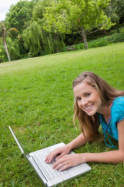 Lachende meisje liggen in een openbare tuin tijdens het werken aan haar lapto — Stockfoto